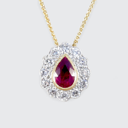 Gold necklace with a teardrop-shaped ruby pendant on a light gray background
