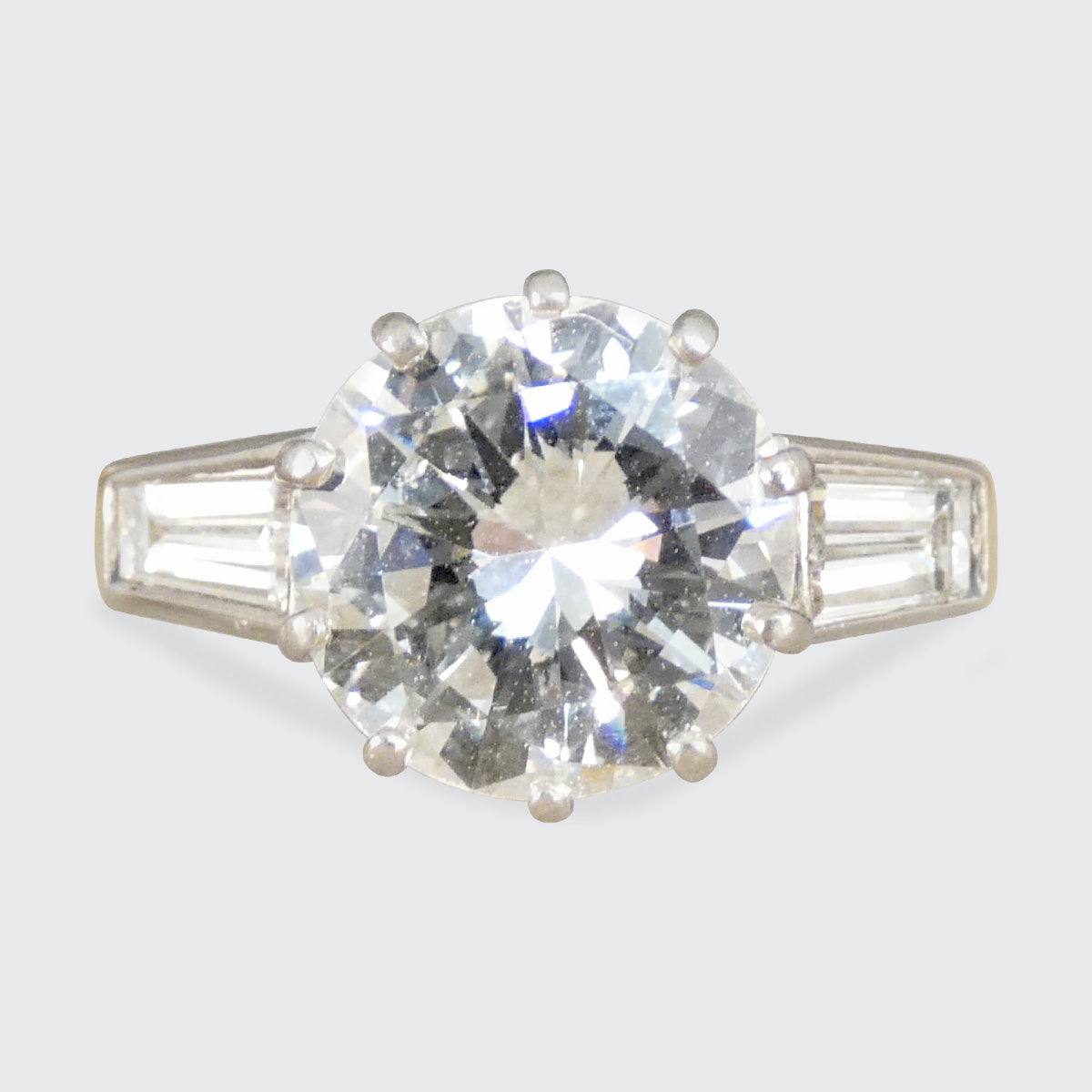 Diamond ring with a large central gemstone and smaller baguette-cut stones on a light gray background