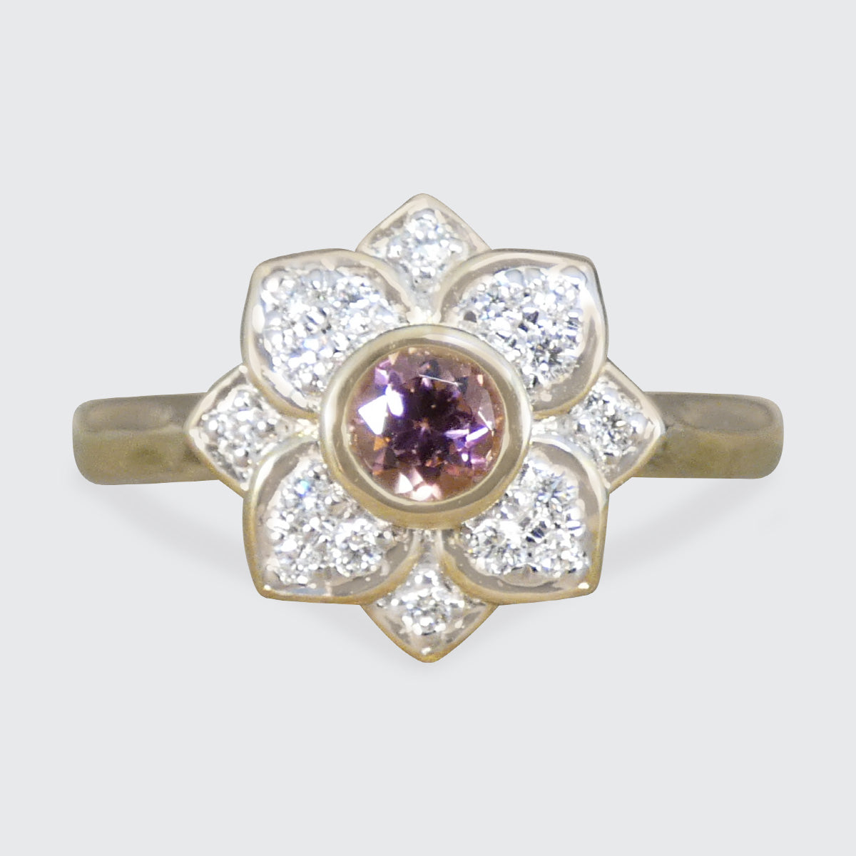 Gold ring with a central pink gemstone and diamond-studded petals on a light gray background