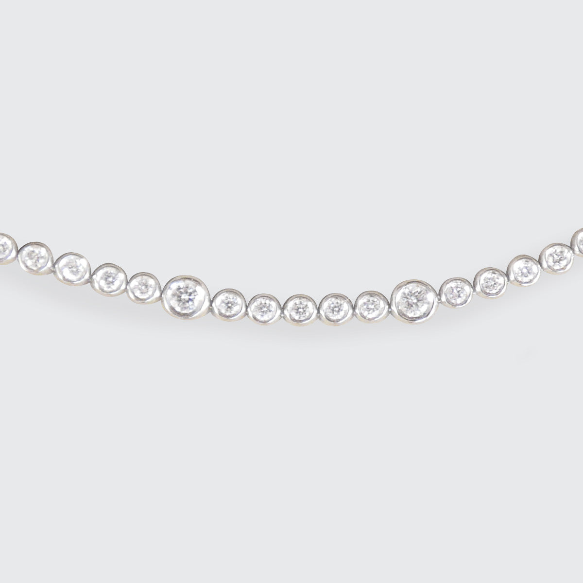 A diamond tennis bracelet in bezel settings at different sizes in 18ct white gold.