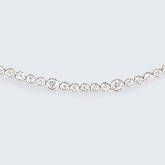 A diamond tennis bracelet in bezel settings at different sizes in 18ct white gold.