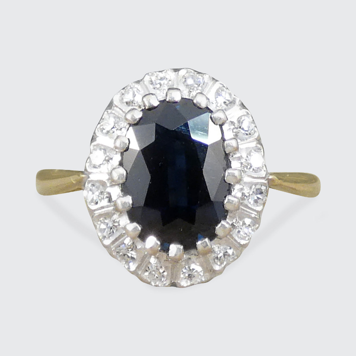 Ring with a central blue gemstone and diamond-studded halo on a white background