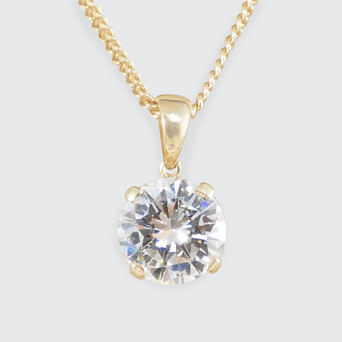 A round-cut clear diamond gemstone pendant in a gold four-prong setting on a gold chain, shown against a light gray background.