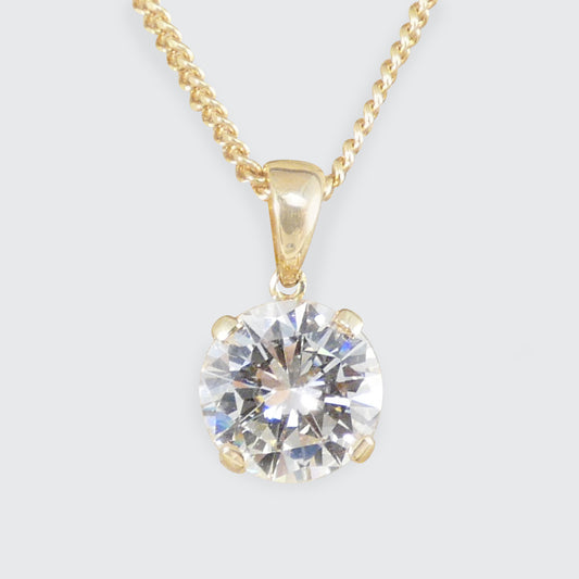A round-cut clear diamond gemstone pendant in a gold four-prong setting on a gold chain, shown against a light gray background.