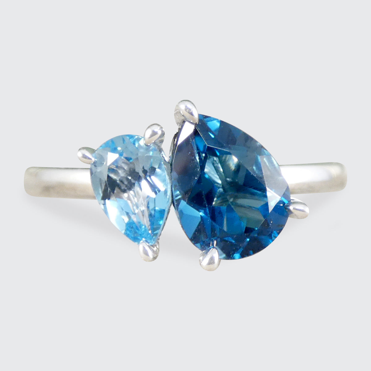 Silver ring with two pear-shaped blue gemstones on a light gray background