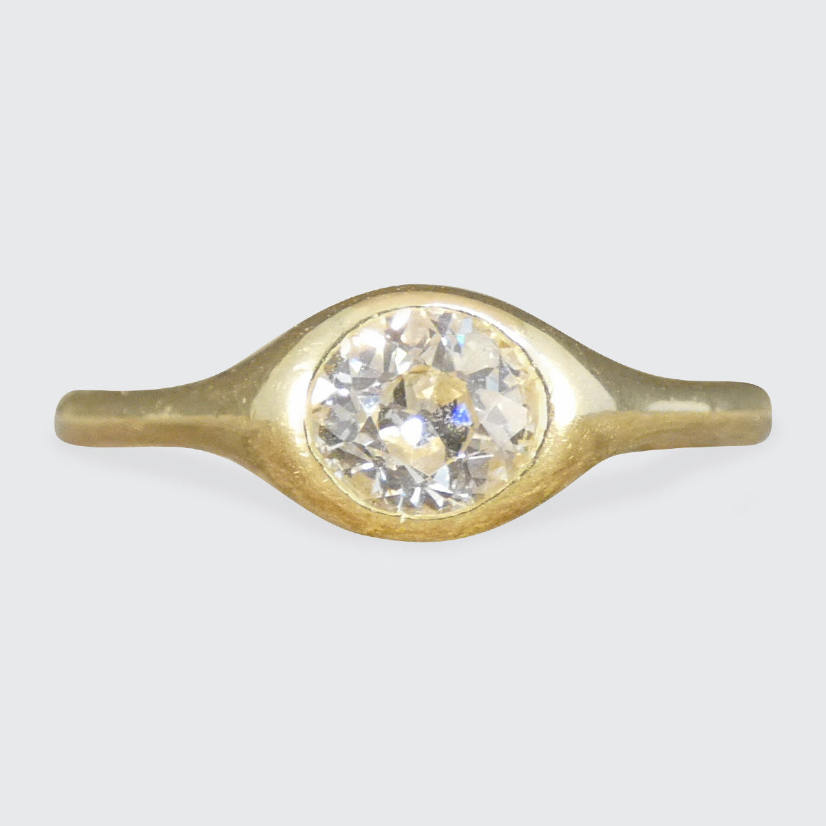 A vintage-style gold ring featuring a large, round clear gemstone in a bezel setting, shown against a neutral light gray background.
