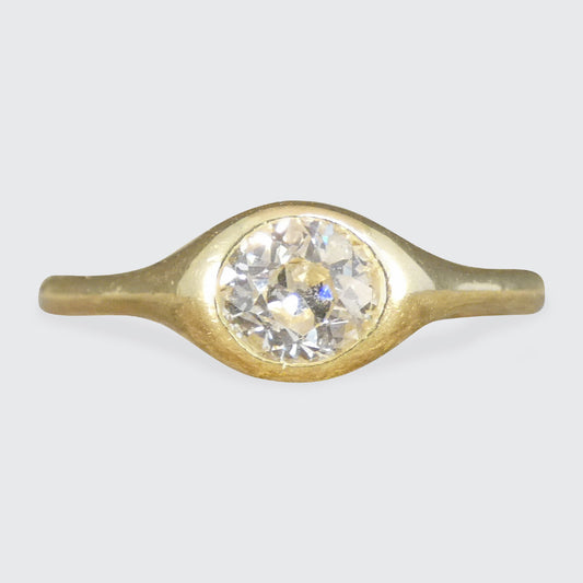 A vintage-style gold ring featuring a large, round clear gemstone in a bezel setting, shown against a neutral light gray background.