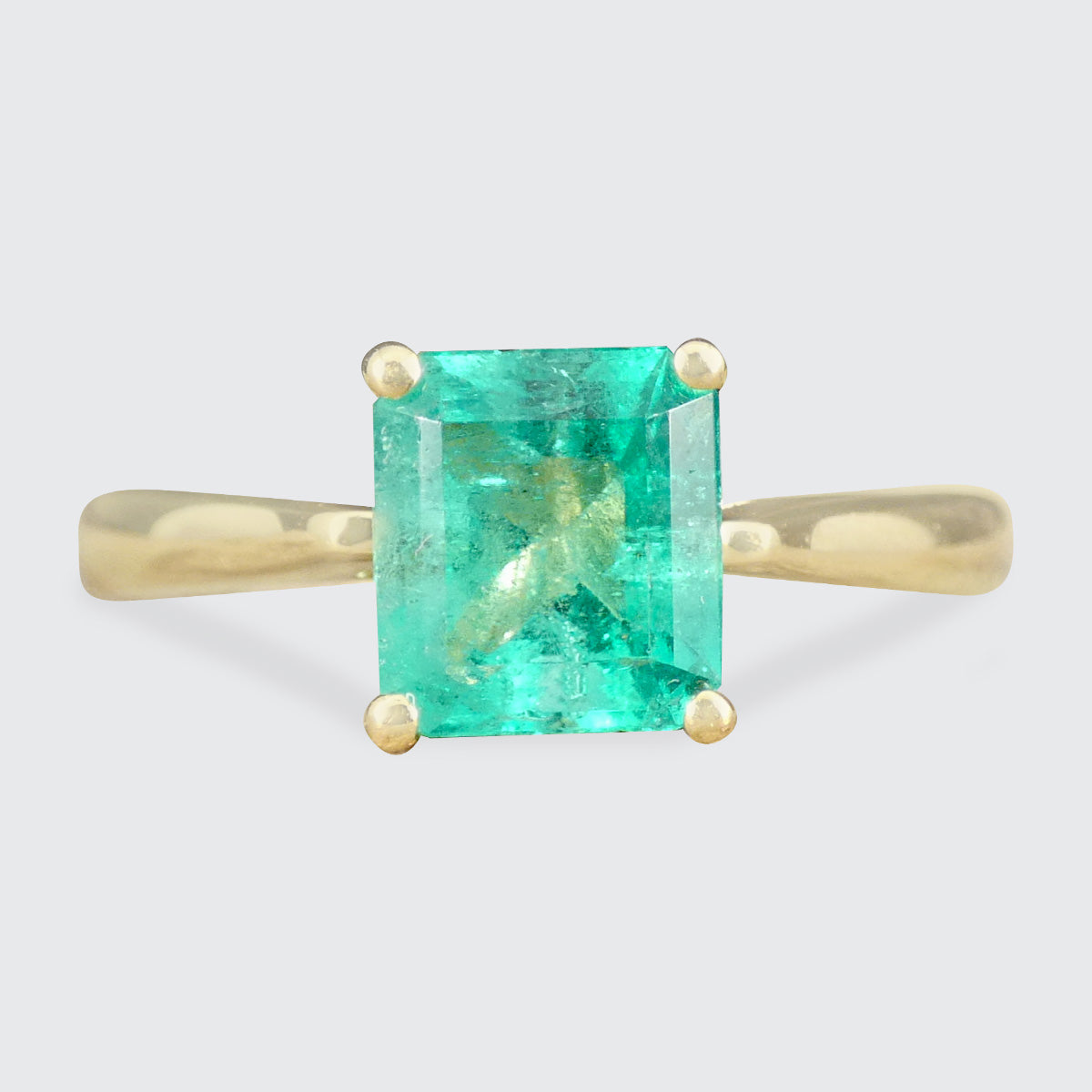 Gold ring with a green gemstone on a light gray background
