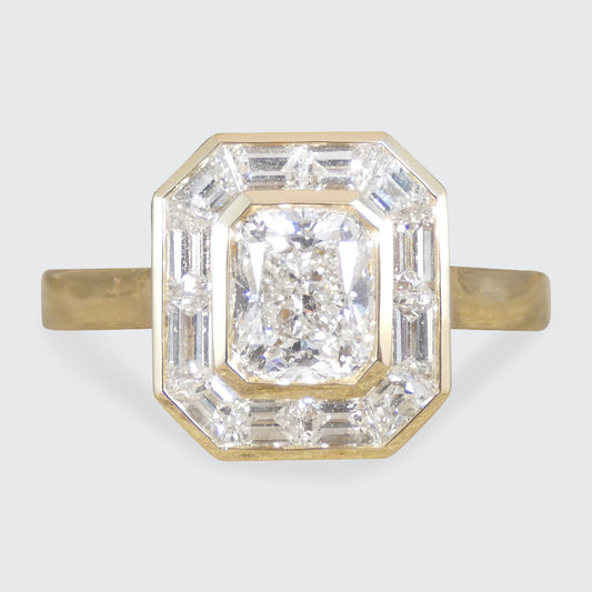 A modern diamond ring featuring a central cushion-cut diamond surrounded by baguette-cut diamonds in a gold-toned setting, with a yellow gold band.