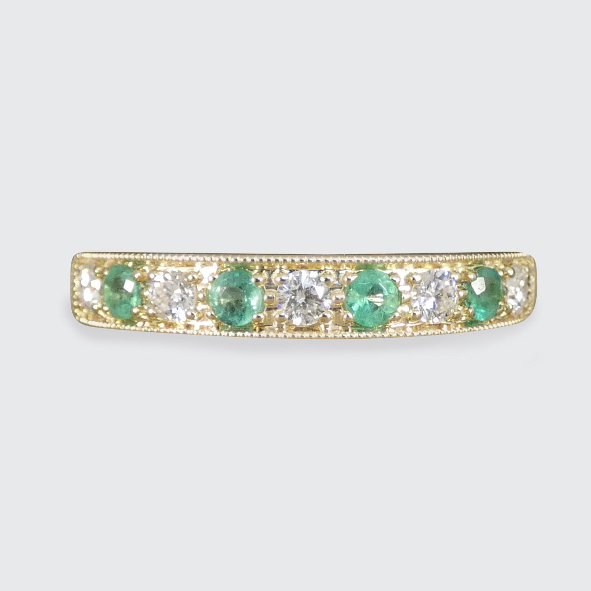 Gold ring with emeralds and diamonds on a light gray background