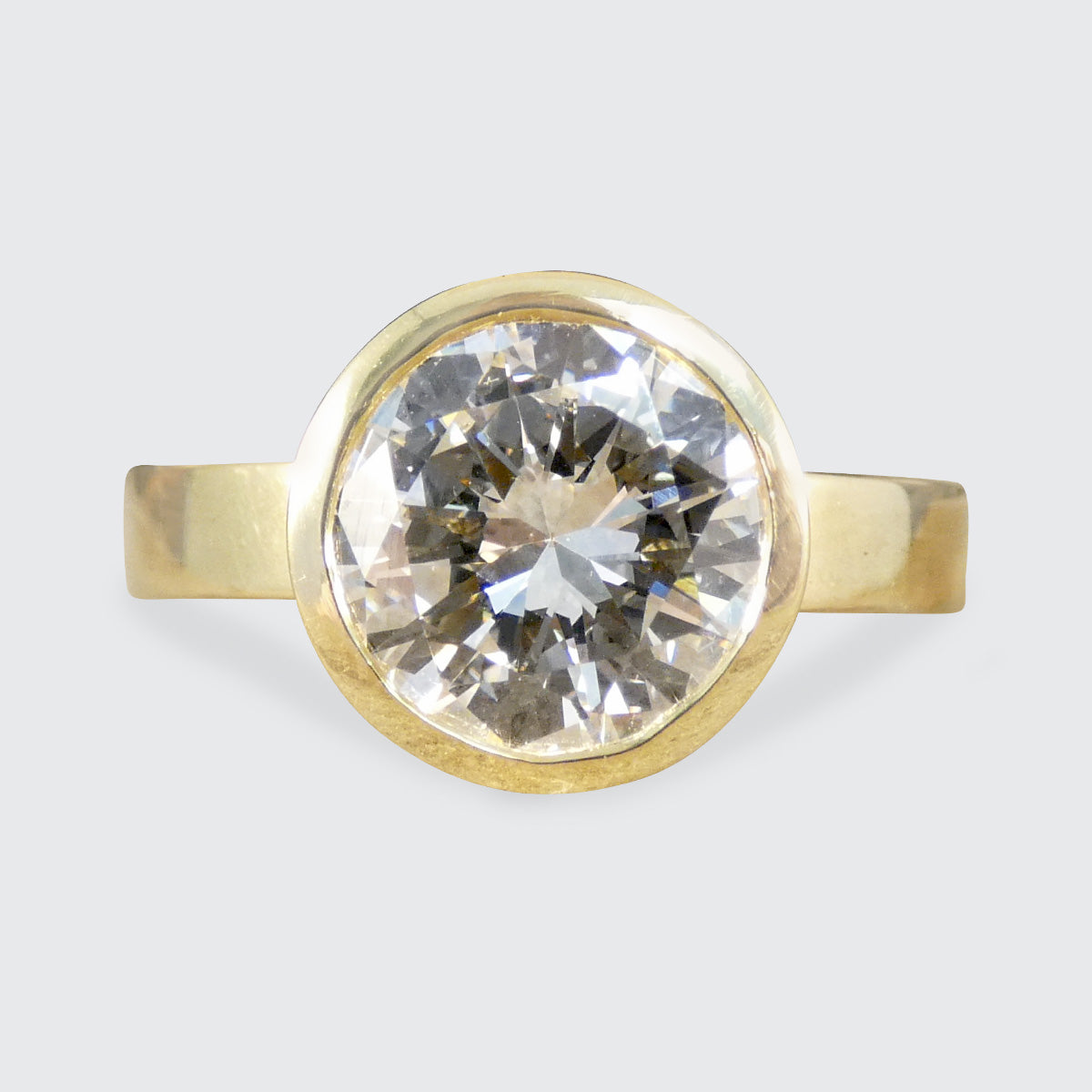 A diamond solitaire ring in a rub over bezel setting in 18ct yellow gold