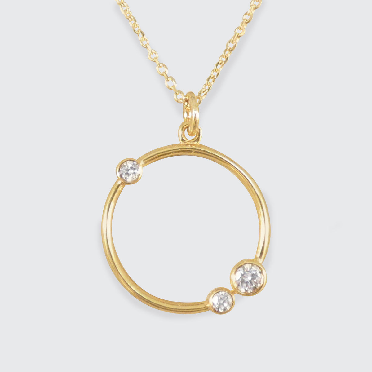 Gold necklace with a circular pendant featuring three diamonds on a light gray background