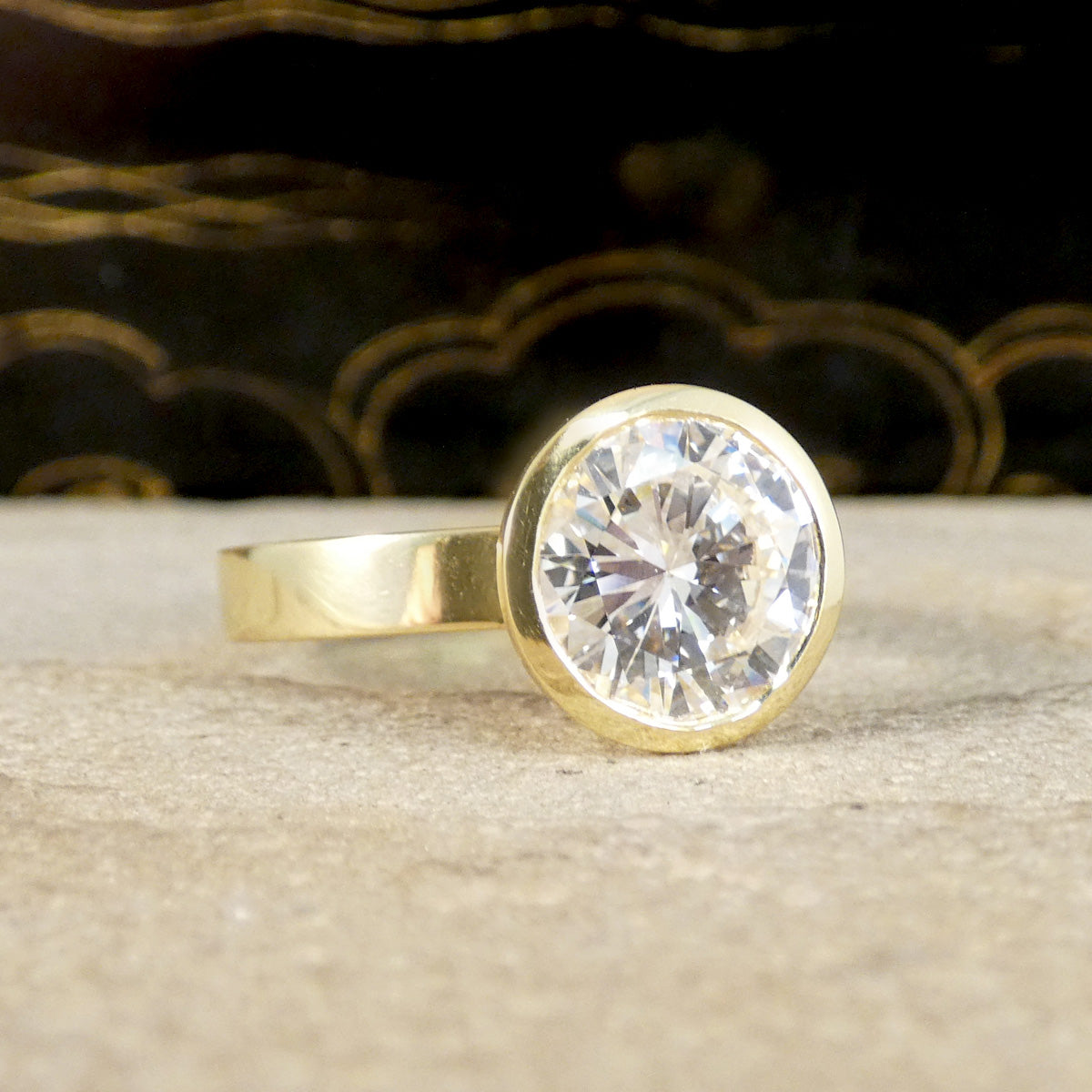 A diamond solitaire ring in a rub over bezel setting in 18ct yellow gold