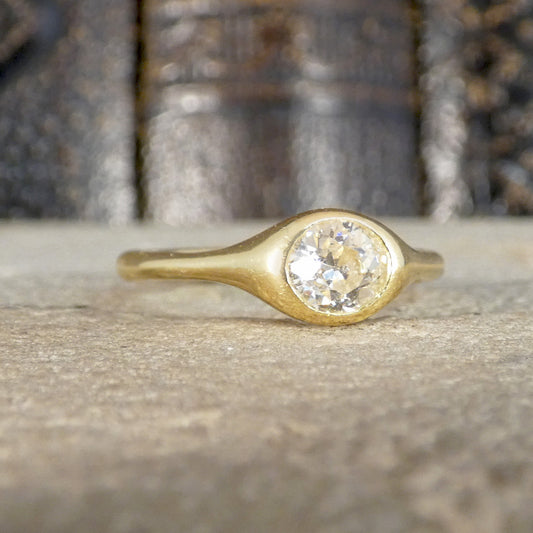 A gold ring with a round clear gemstone set in a bezel-like oval, resting on a textured stone surface with a blurred background.