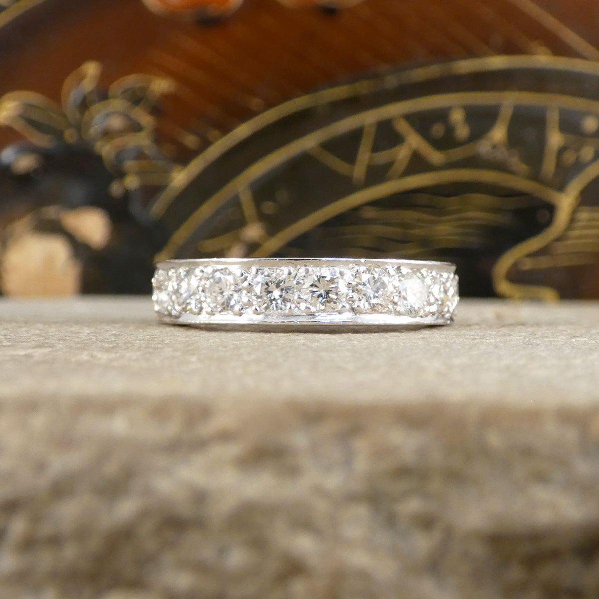 A full diamond eternity ring in 18ct white gold. Displayed on an ornate background