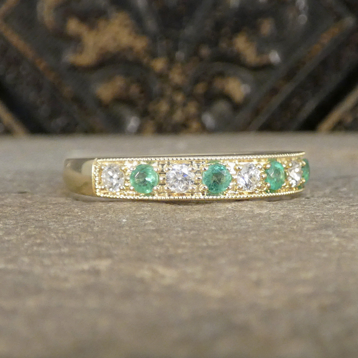 Gold ring with emeralds and diamonds on a textured surface
