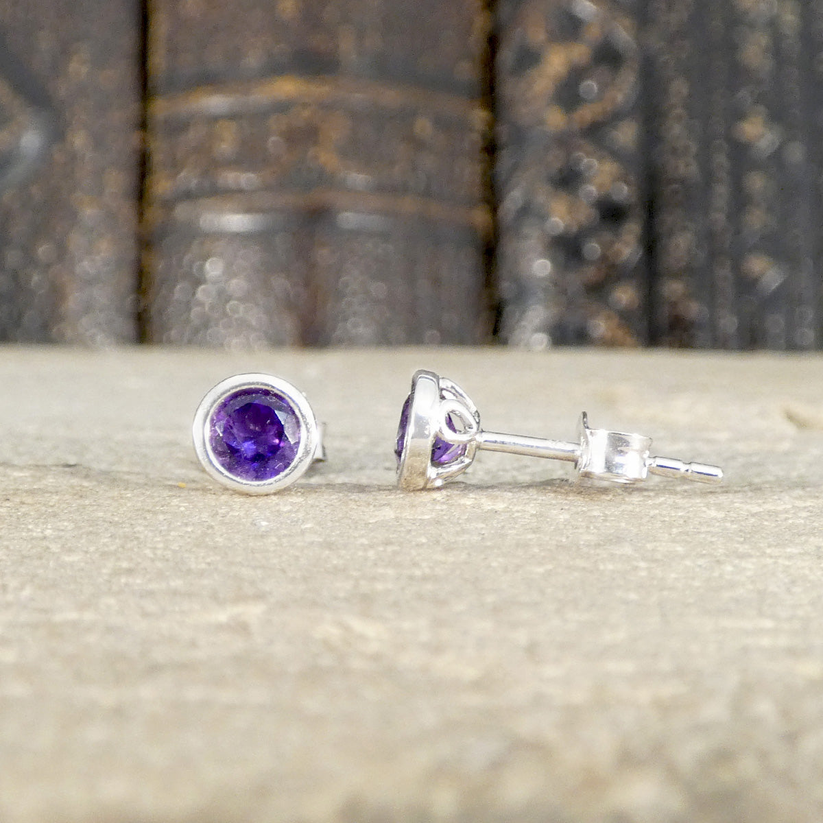 Pair of white gold stud earrings with amethyst gemstones on a textured surface.