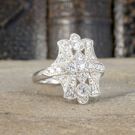 An Art Deco style platinum ring featuring a starburst-shaped cluster of clear round and oval gemstones, photographed resting on a textured stone surface with a blurred dark background.