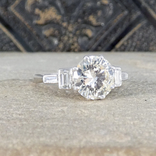 Diamond ring with a large central diamond and smaller baguette-cut stones on a stone surface.
