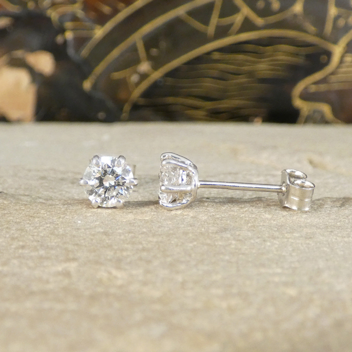 A pair of diamond stud earrings with six claws, one shown from the front and the other from the side.