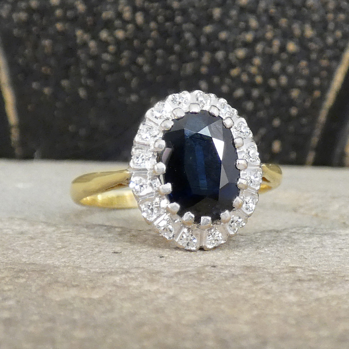 Gold ring with a blue gemstone and diamond halo on a textured surface