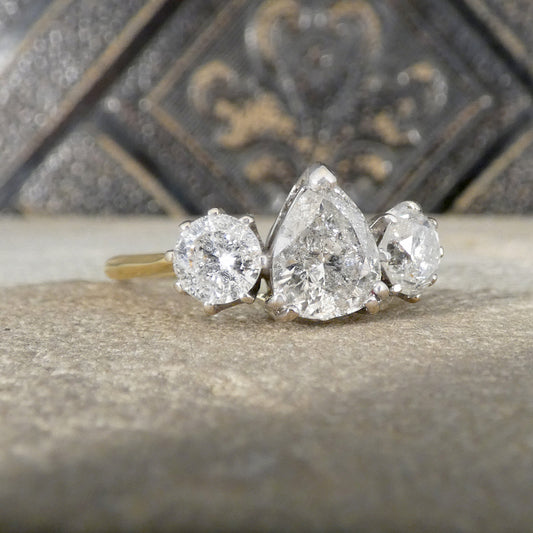 Three-stone diamond ring with pear-shaped center stone on a textured surface.