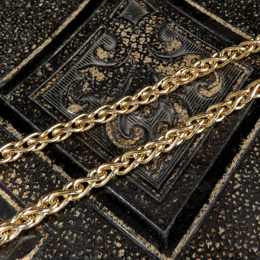 A close-up of a polished gold chain draped diagonally across a dark, textured embossed surface.