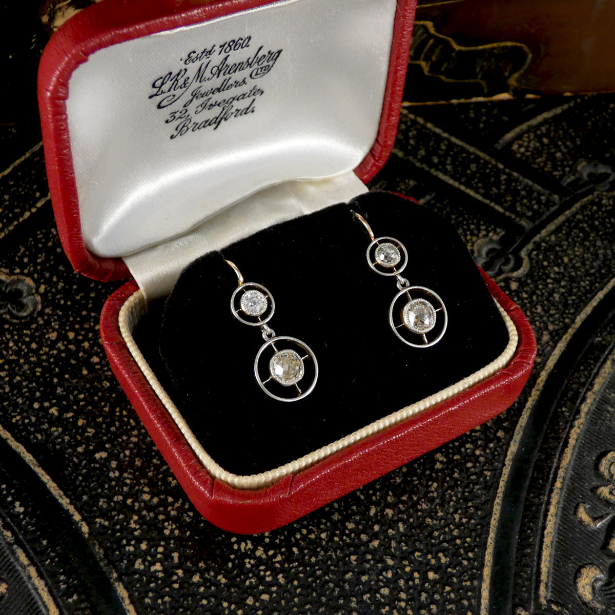 Diamond earrings in a red and white jewelry box on an ornate surface