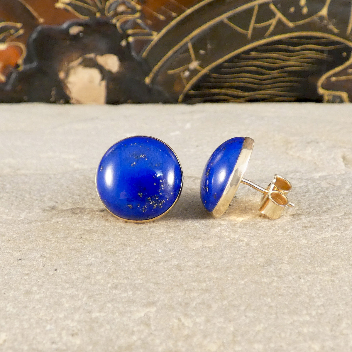 a pair of large blue Lapis Lazuli stud earrings in 9ct yellow gold, shown one from the front and one from the side.