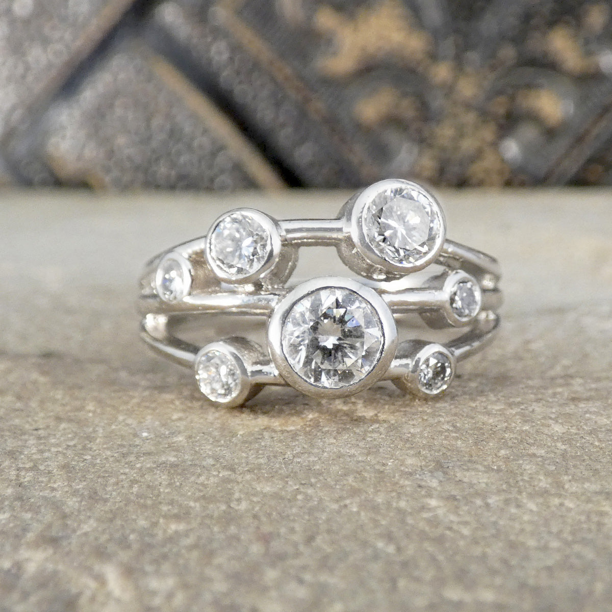 A silver ring with multiple round clear gemstones in a branching, organic design, resting on a textured stone surface.