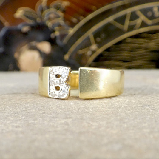 Gold ring with letter 'B' on a textured surface