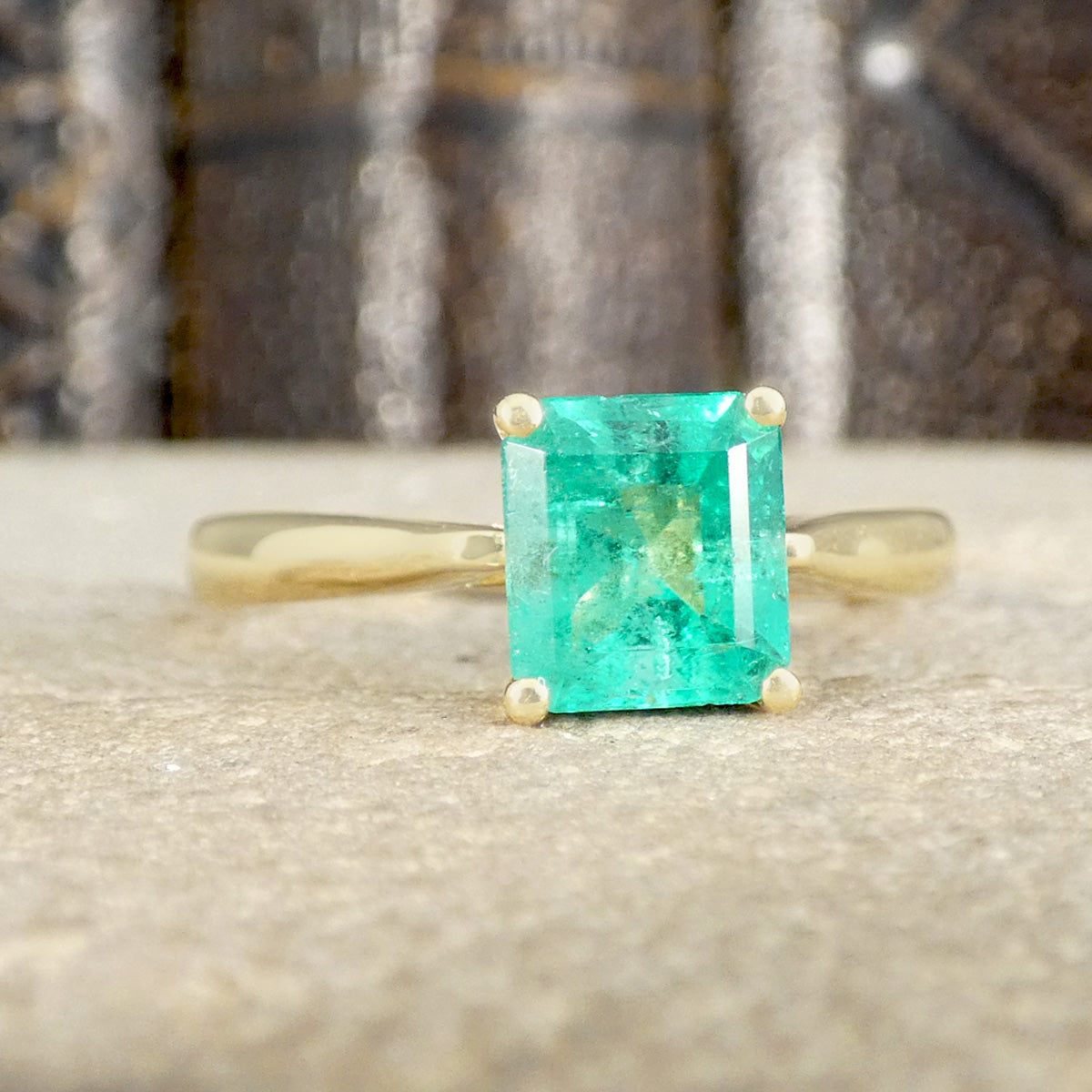 Gold ring with a green emerald stone on a textured surface