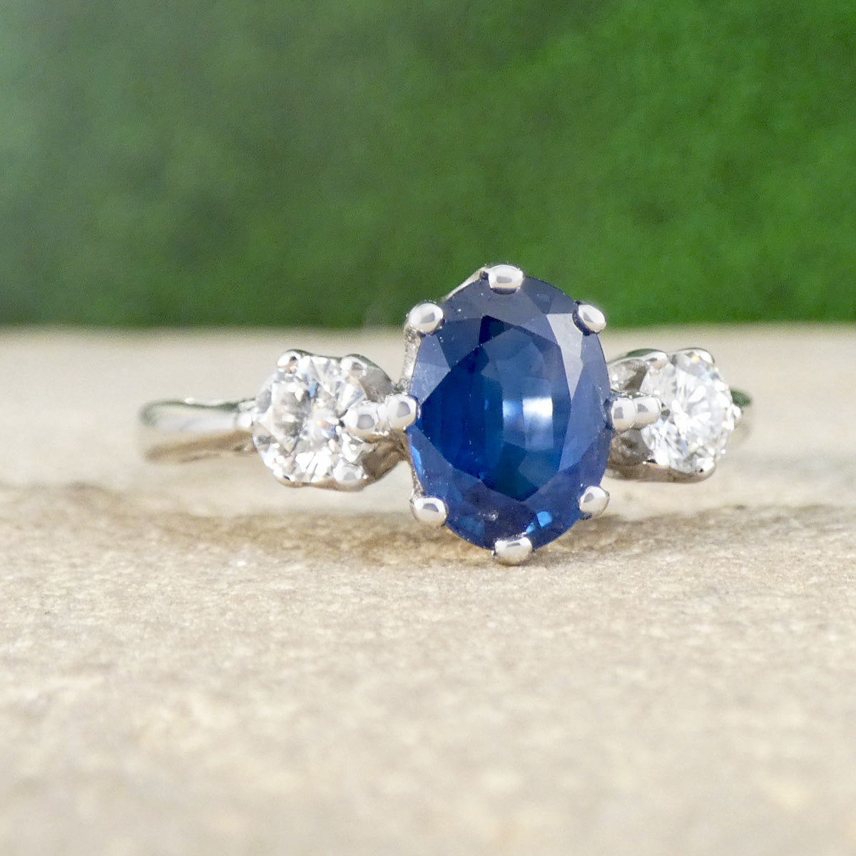 Ring with a blue gemstone and diamond accents on a textured surface with a green background