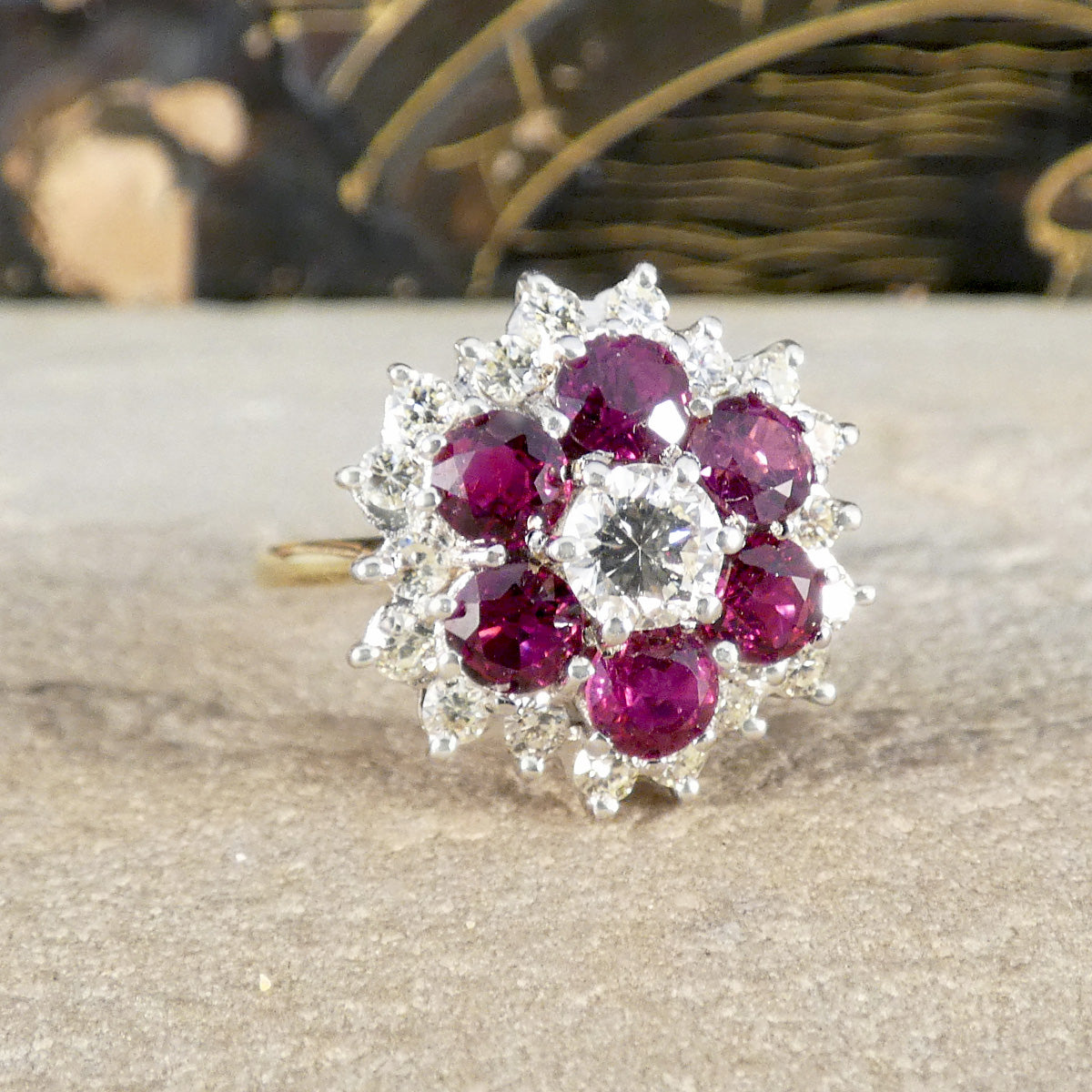 A diamond and Ruby cluster ring shown on an ornate background.
