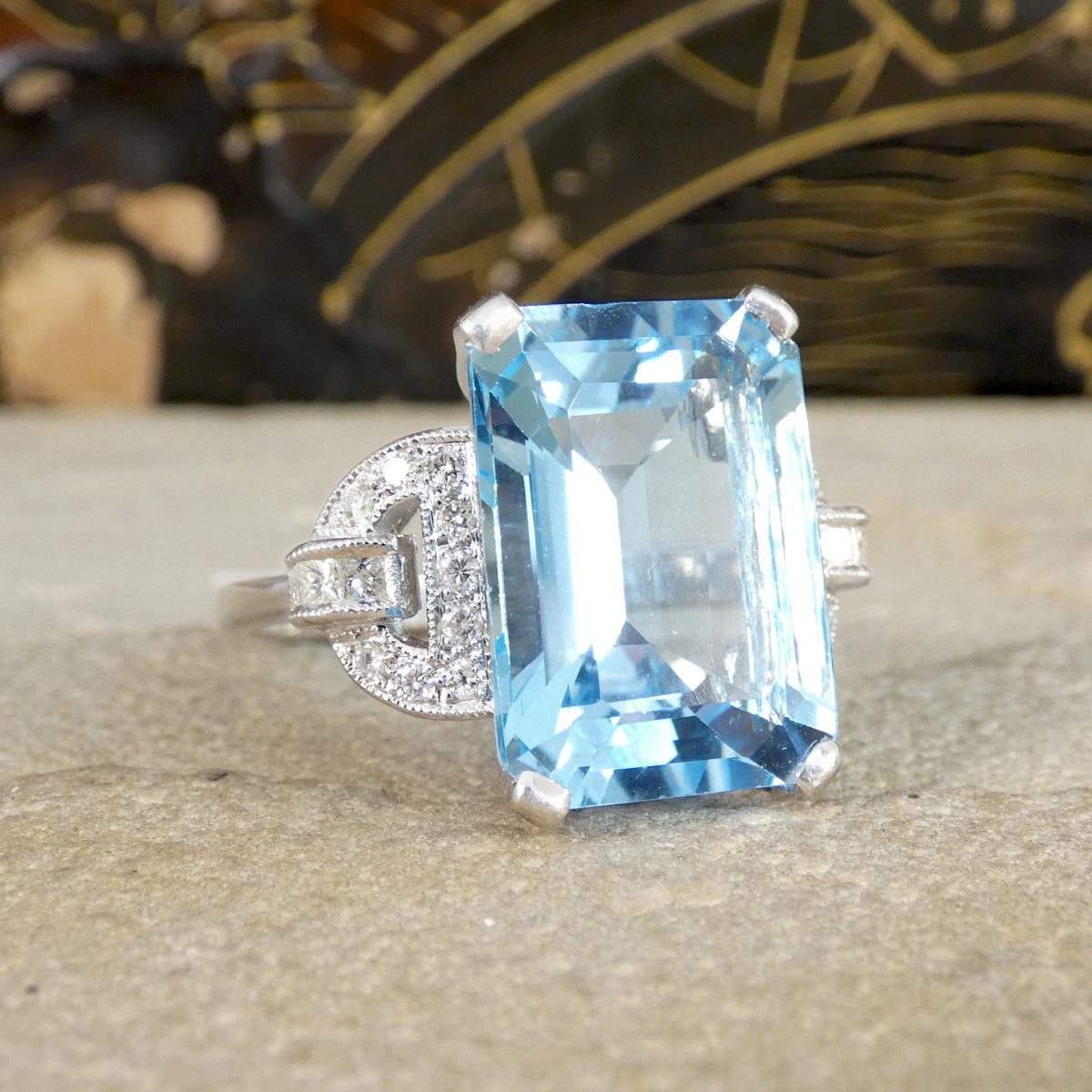Ring with a large blue topaz gemstone with diamond shoulders on a textured surface