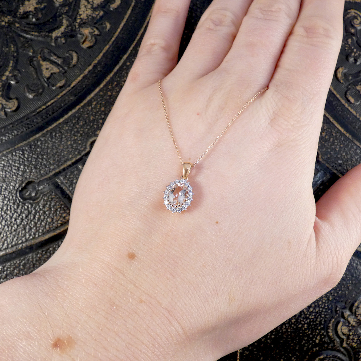 Rose gold necklace with a diamond and morganite pendant on a hand against a dark textured background