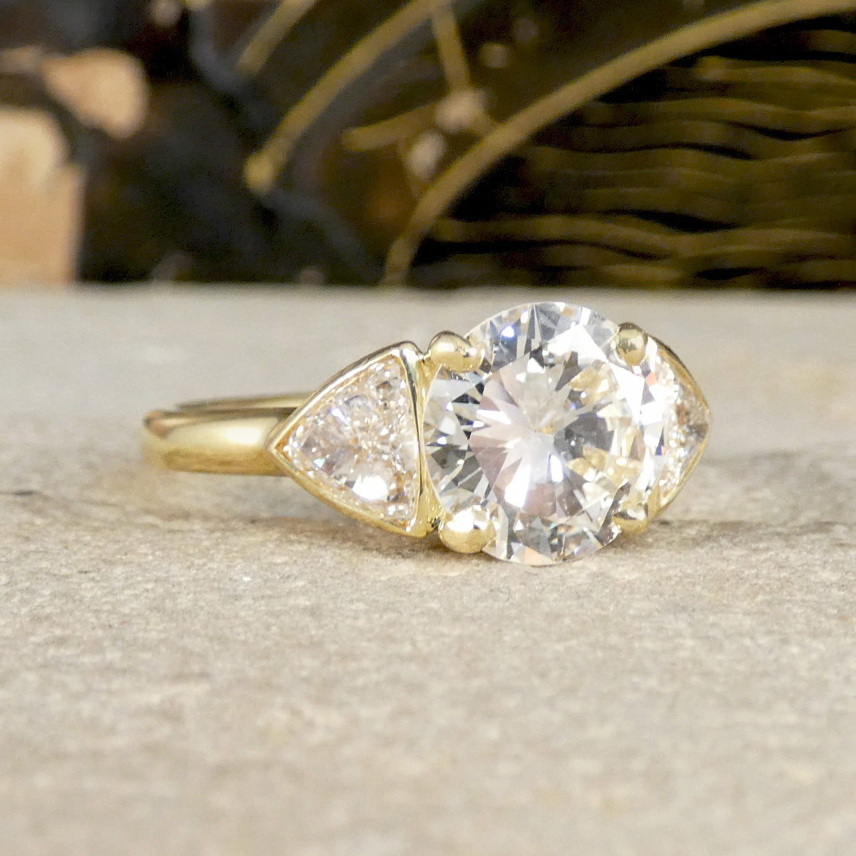 Gold ring with a large diamond and smaller trillion-shaped diamonds on a neutral background