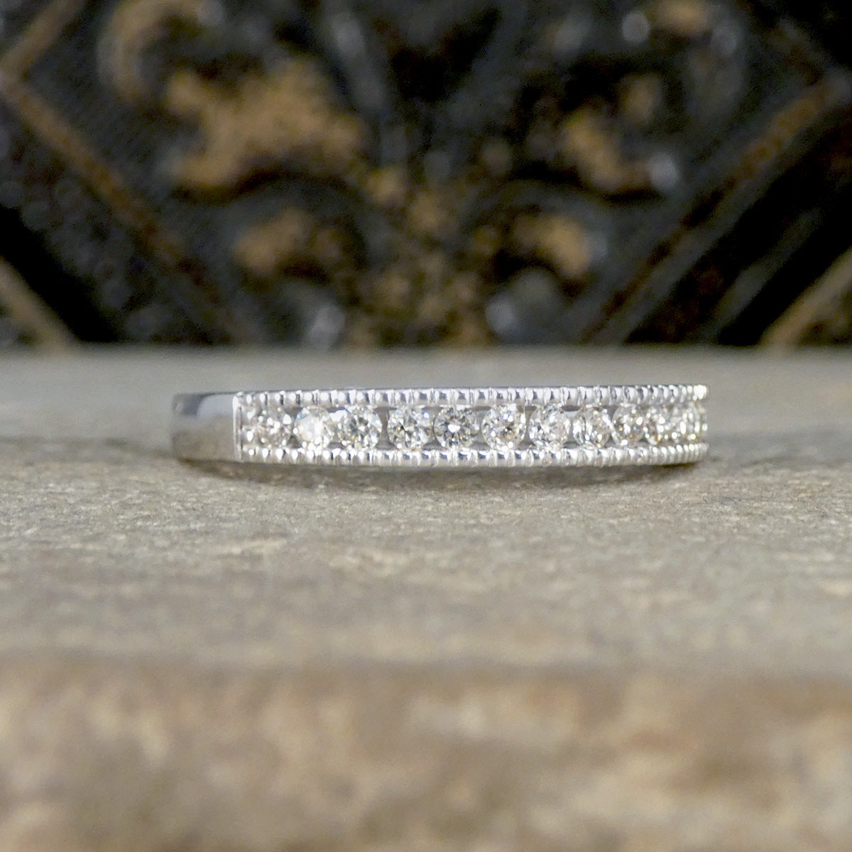 Diamond-studded ring on a textured surface with a blurred decorative background