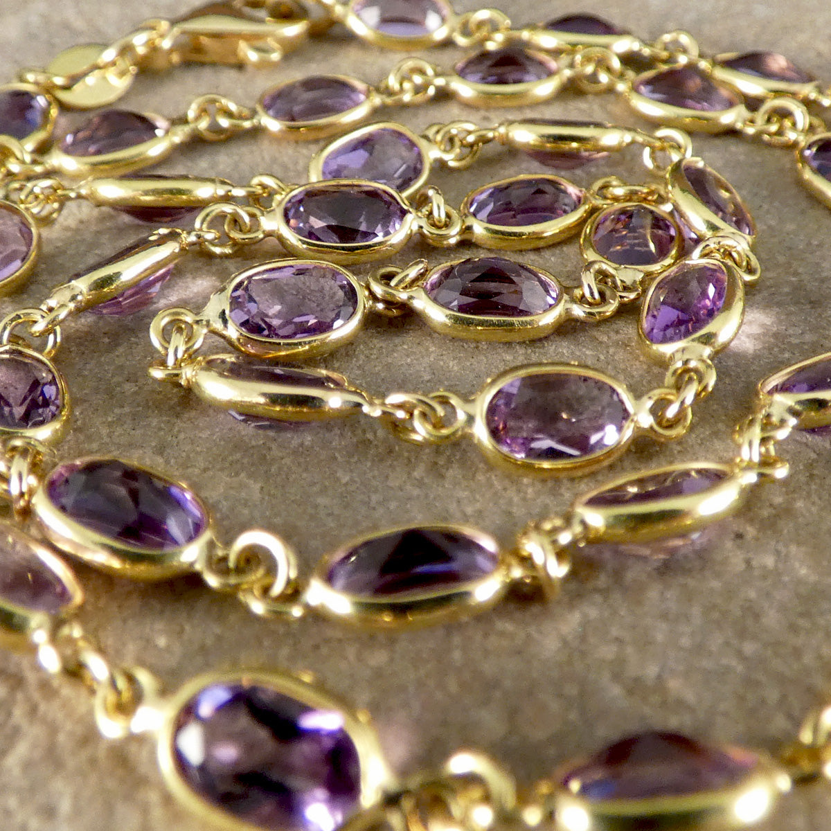 Gold chain with purple gemstones on a textured surface