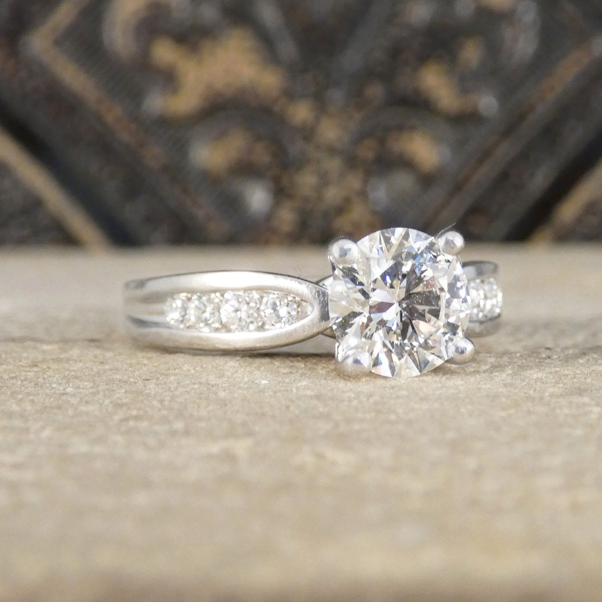 Diamond engagement ring on a textured surface with a blurred decorative background
