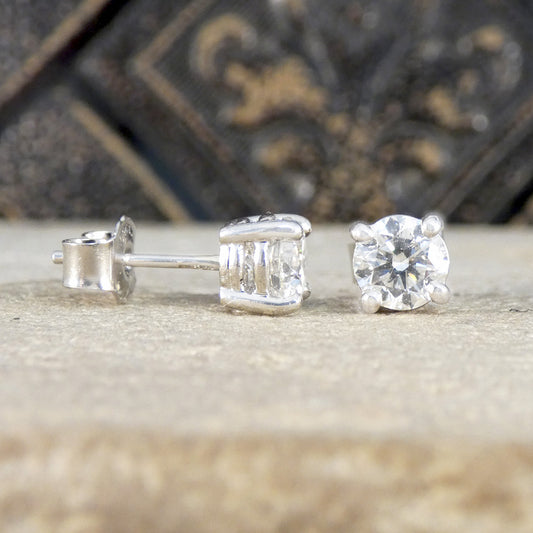 Diamond stud earrings on a textured surface with a decorative background. 1.40ct total, G/VS grading natural diamonds in Platinum.