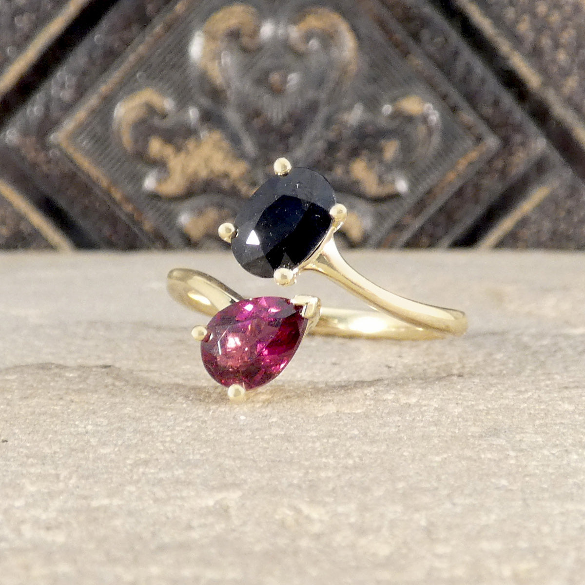 Gold ring with a black gemstone and a pink gemstone on a textured surface.