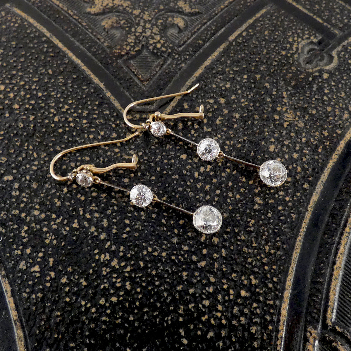 Pair of gold earrings with diamond gemstones on a textured black surface