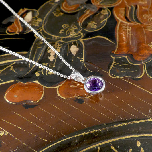 Silver necklace with a purple gemstone pendant on an ornate wooden surface