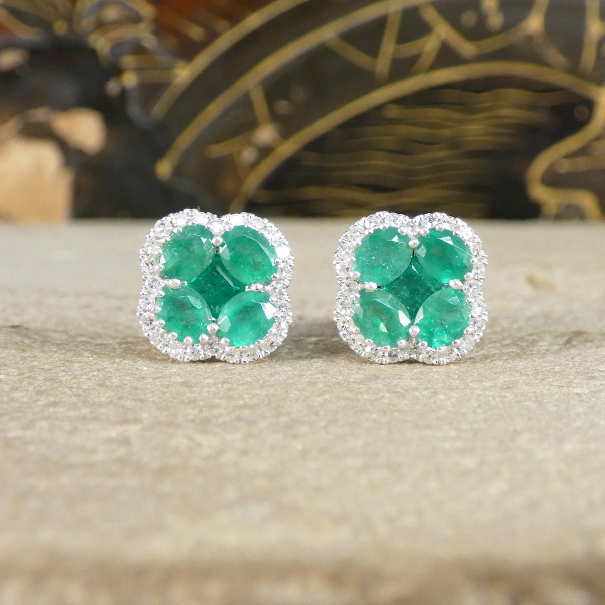 Pair of emerald earrings on a textured surface with a blurred decorative background