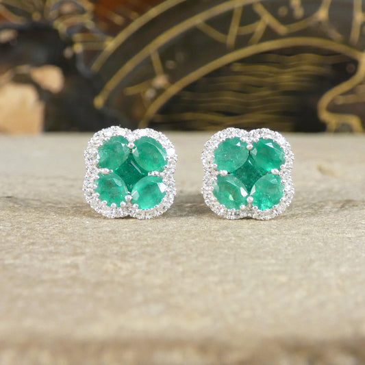 Pair of emerald earrings on a textured surface with a blurred decorative background