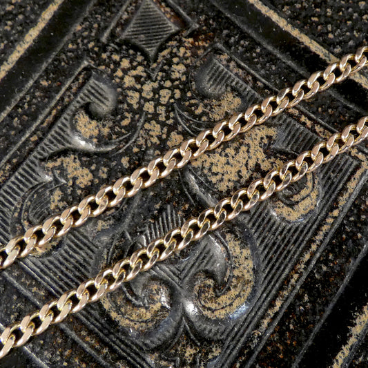 Two gold-toned metal chains laid diagonally across a dark, ornate textured surface with raised decorative patterns.