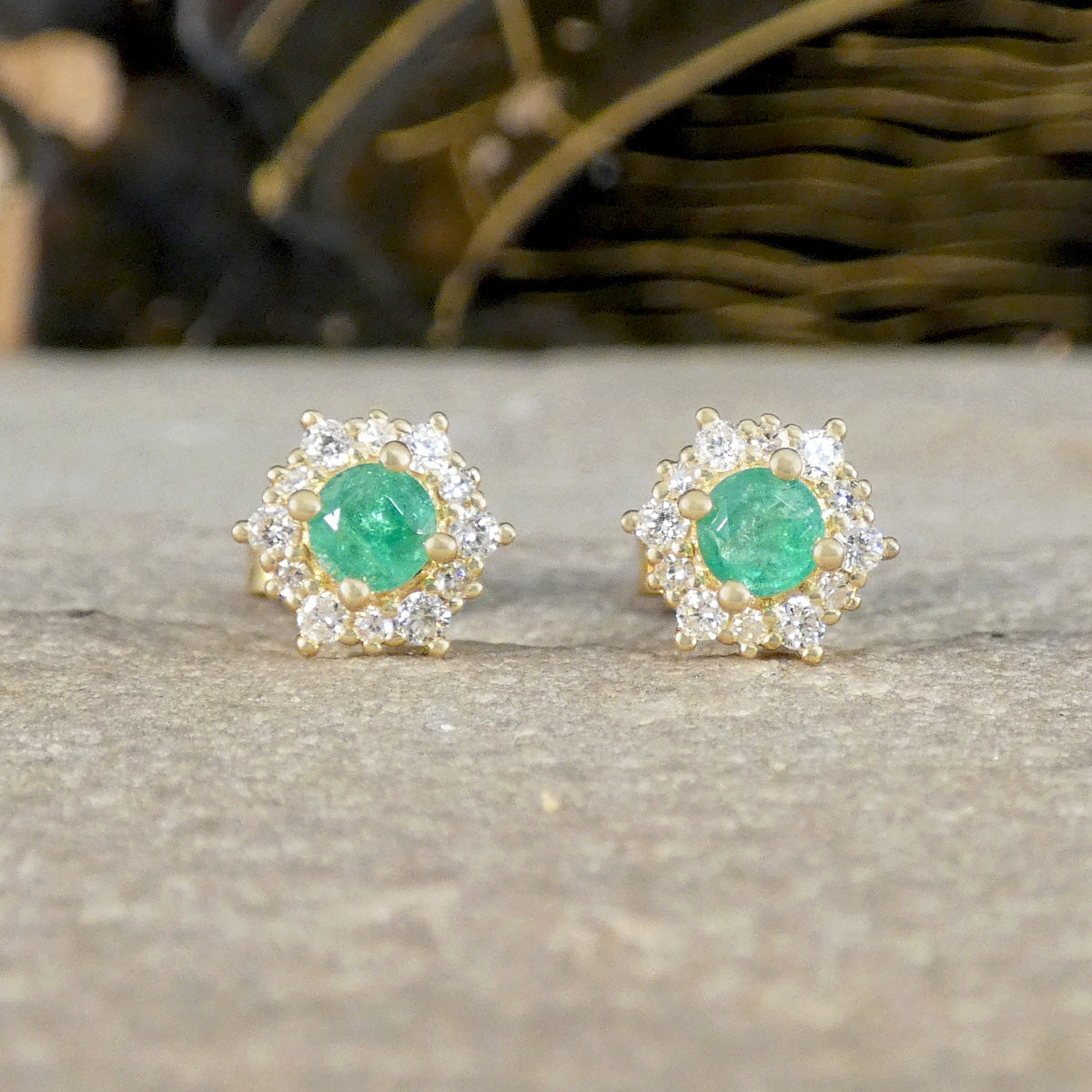 Pair of emerald and diamond stud earrings on a neutral background