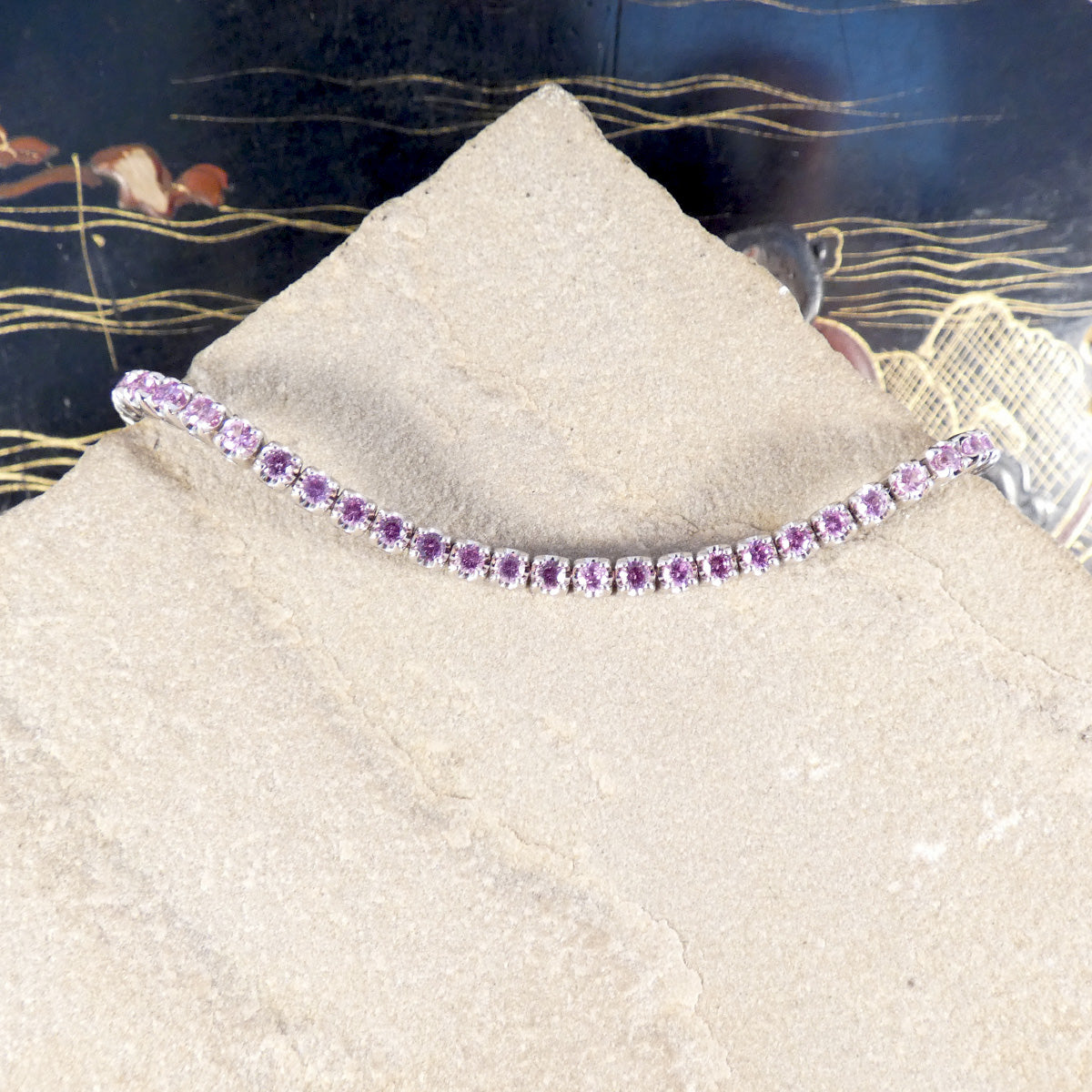 A pink sapphire and diamond tennis bracelet in white gold displayed on a stone