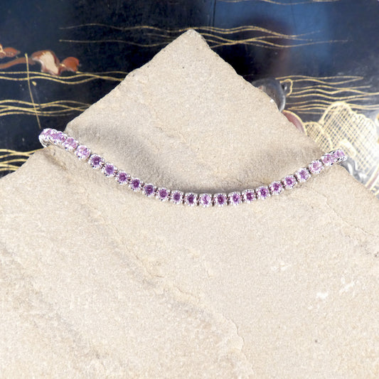 A pink sapphire and diamond tennis bracelet in white gold displayed on a stone
